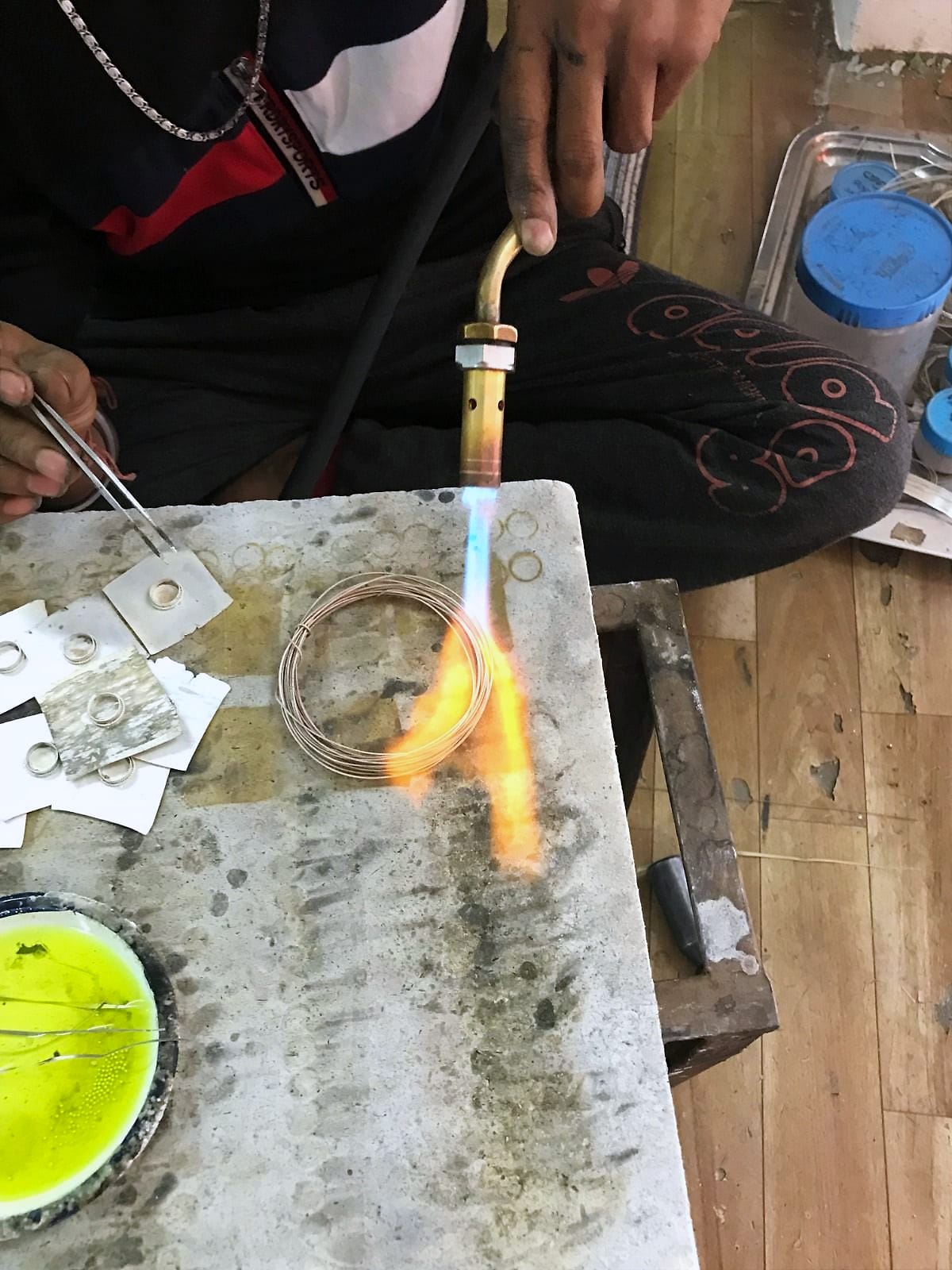 A torch flame heats a coil of silver wire on a soldering block